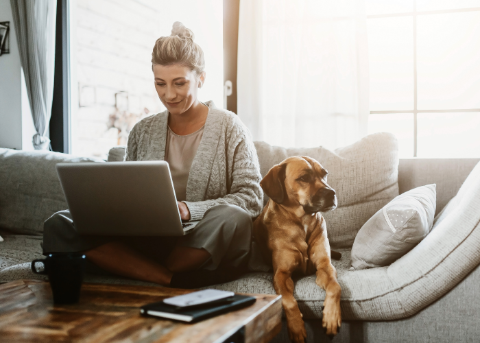 Lady using a laptop on a couch with a dog sitting next to her