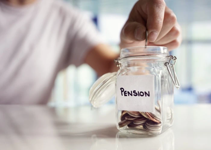 A hand putting coins in a glass jar with a sticker that says "pension"